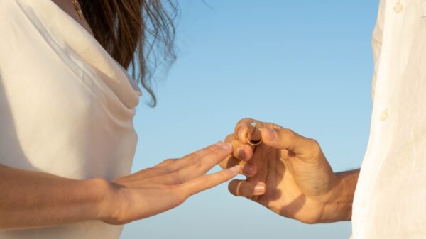 fotografia de uma mão feminina esticada e uma mão masculina colocando uma aliança nela em céu aberto