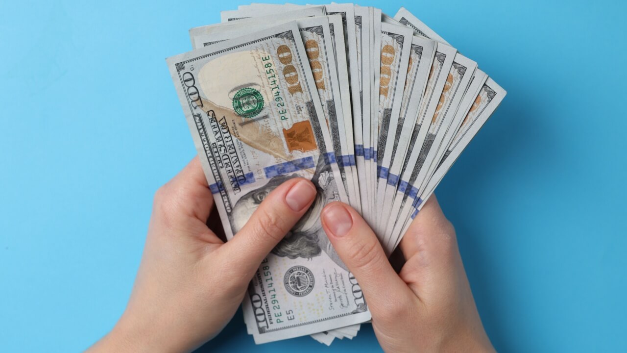 mão segurando um leque de dólares em fundo azul