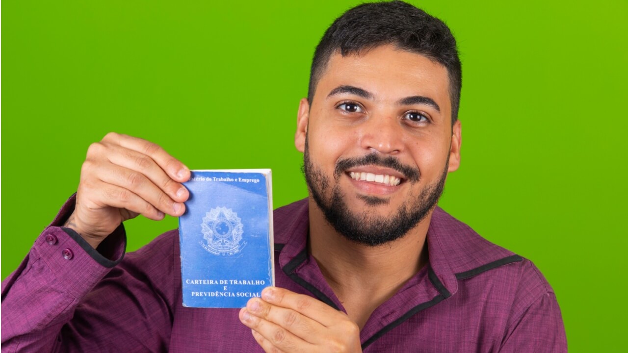 Homem segurando uma Carteira de Trabalho e Previdência Social.