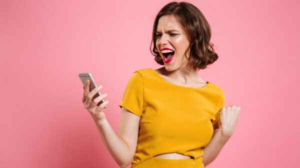 mulher comemorando com um celular na mão em fundo rosa