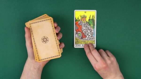 mão esquerda segurando um baralho de tarot e mão direita segurando apenas uma carta em fundo azul