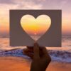 pôr do sol na praia com um cartão com um coração vazado