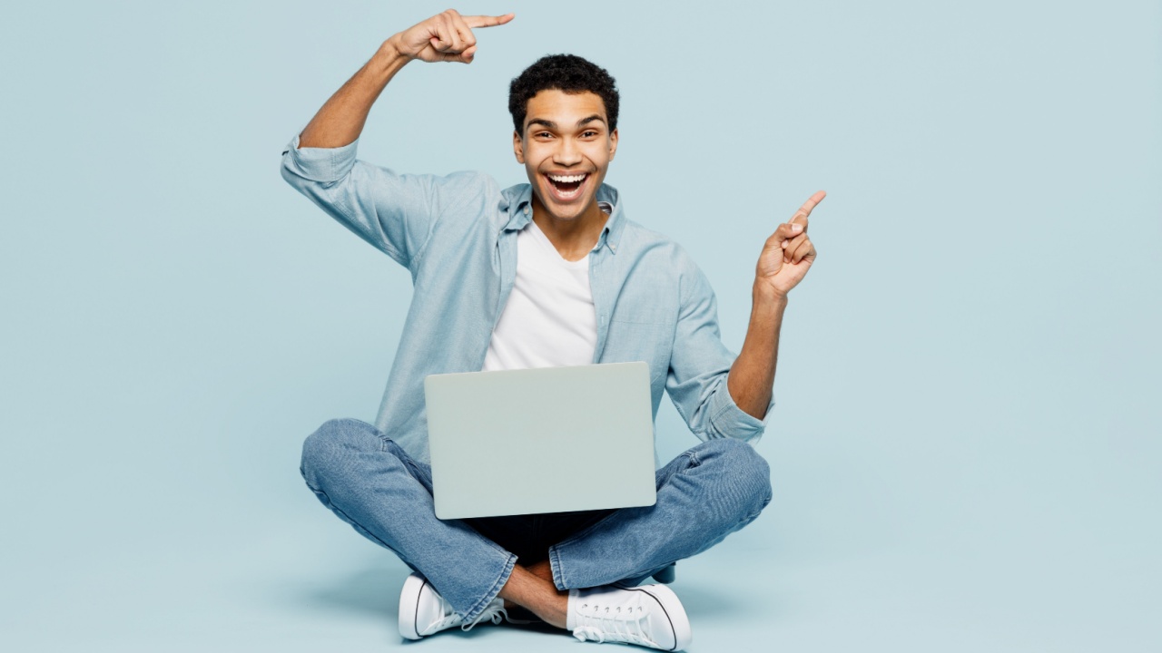 homem com expressão de animação e um notebook no colo em fundo azul claro