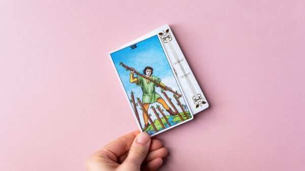 mão segurando uma carta de tarot em fundo rosa claro