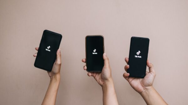 três mãos segurando cada um celular cada um com o aplicativo tiktok aperto em fundo rosinha
