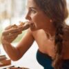 mulher sentada em restaurante com um pedaço de pizza na mão mordendo