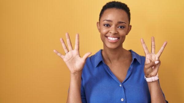 mulher negra fazendo o número oito com os dedos em fundo amarelo escuro