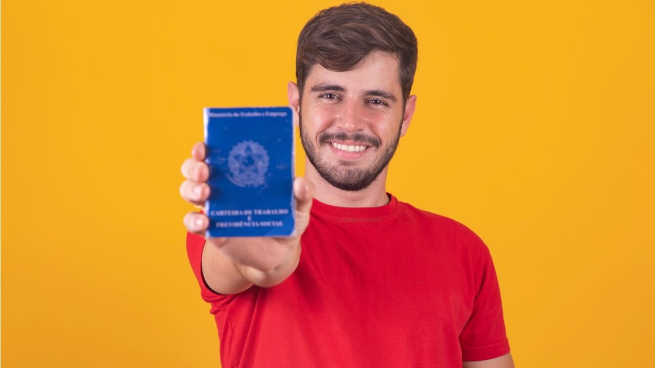 Homem segurando uma Carteira de Trabalho e Previdencia Social.