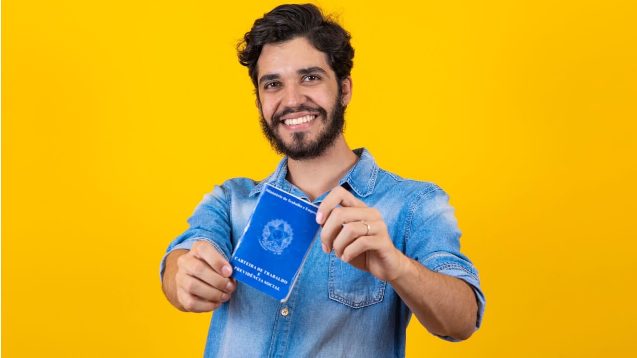 Homem segurando uma Carteira de Trabalho e Previdência Social.