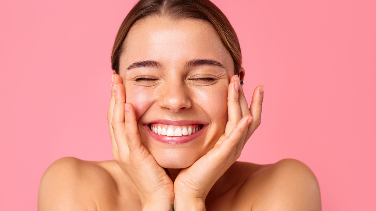 mulher sorrindo e com as mãos apoiadas no queixo em fundo rosa