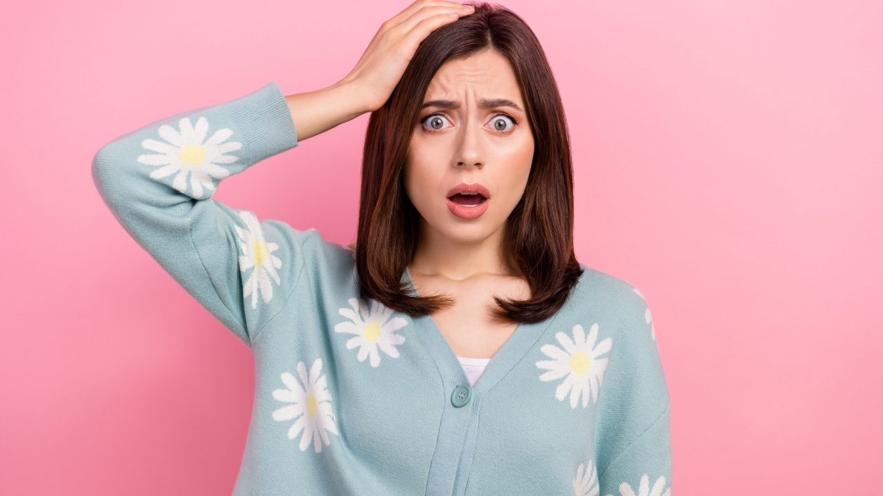 mulher com a mão na cabeça e expressão facial de assustada em fundo rosa