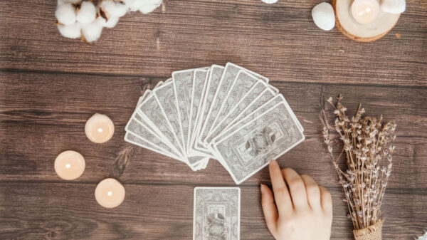 baralho de tarot distribuído em uma mesa de madeira com uma mão escolhendo uma carta