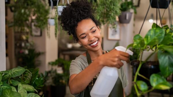 mulher negra sorrindo e regando planta numa sala cheia de plantas e flores