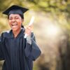 mulher de beca e capelo com diploma na mão gritando de felicidade