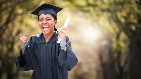 mulher de beca e capelo com diploma na mão gritando de felicidade