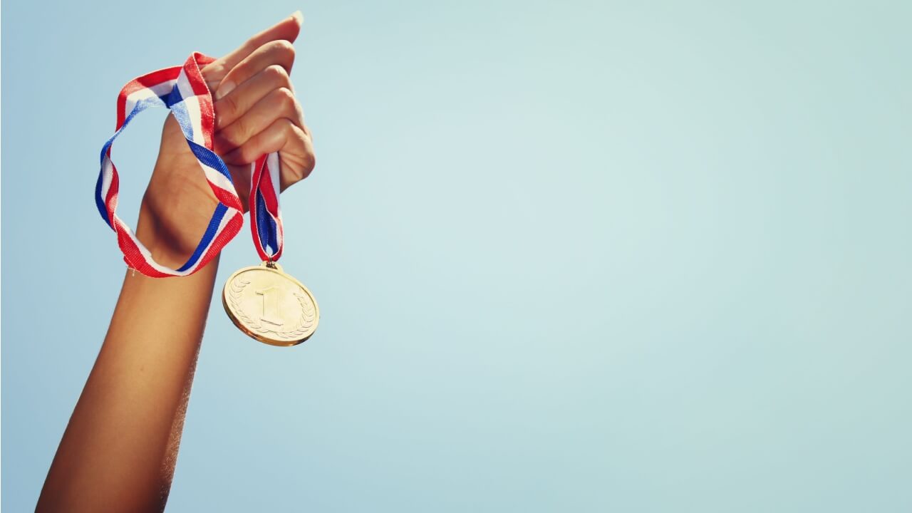 Mão de uma mulher levantada, segurando uma medalha de ouro contra o céu. Conceito de prêmio e vitória.