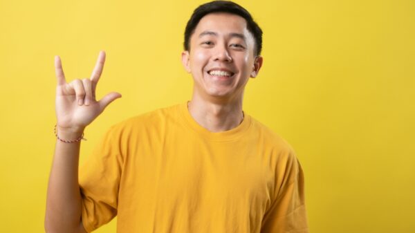 homem jovem com traços asiáticos fazendo um sinal de eu te amo em libra em fundo amarelo