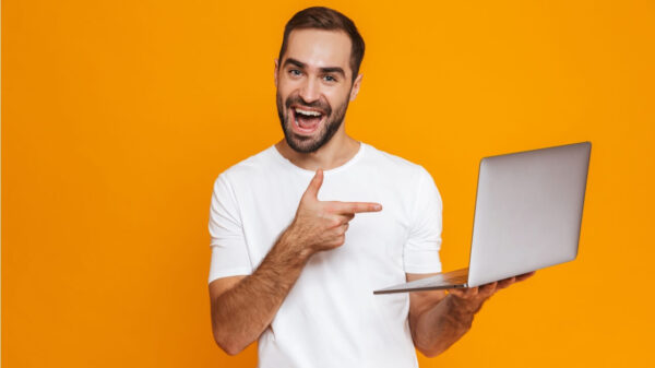 Retrato de um homem usando uma camiseta branca, segurando um laptop cinza, isolado sobre um fundo laranja.