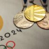 imagem das medalhas de ouro, prata e bronze em cima de um papel branco com o logo das olimpíadas de paris