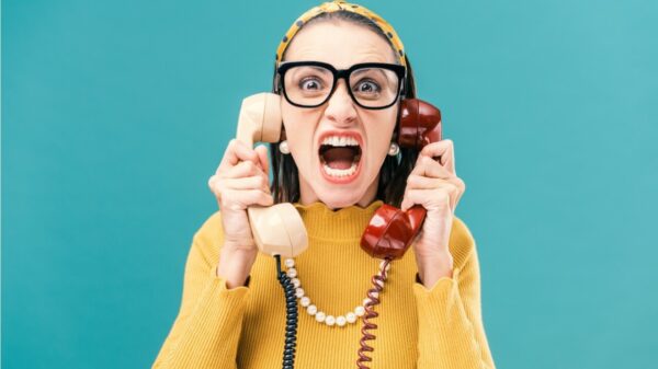 Mulher segurando dois telefones e gritando, estressada e com raiva.