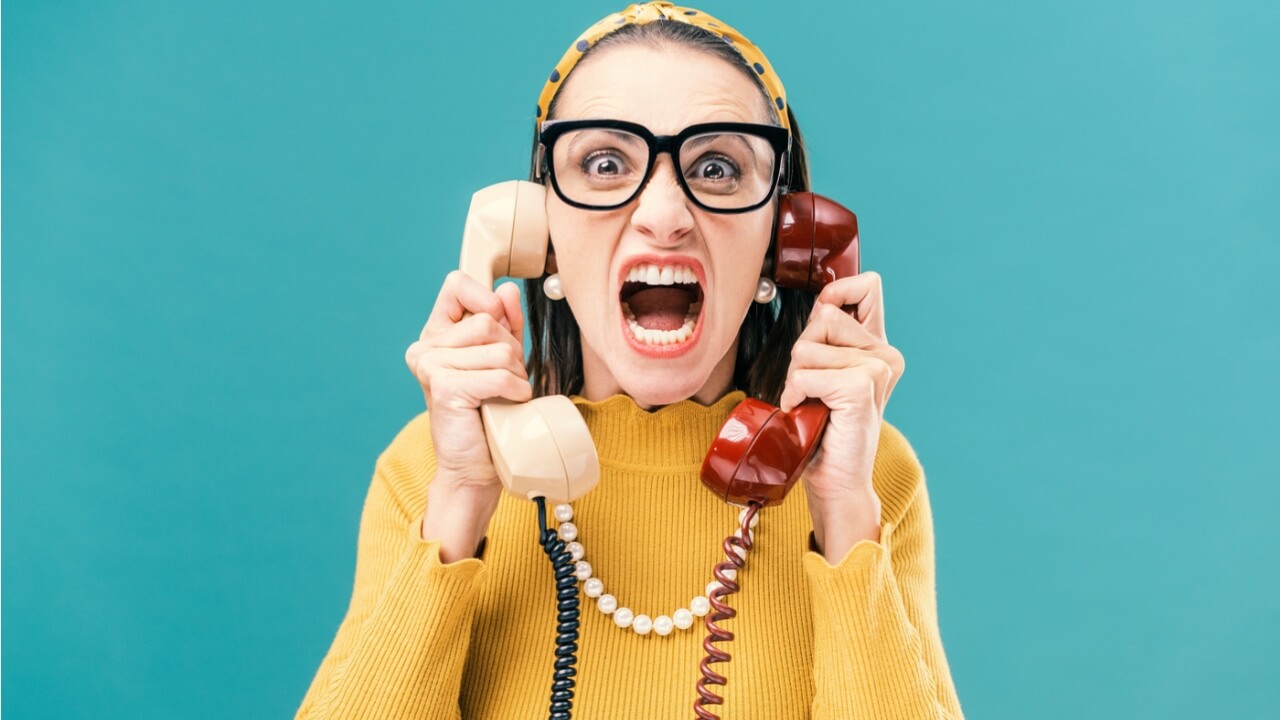 Mulher segurando dois telefones e gritando, estressada e com raiva.