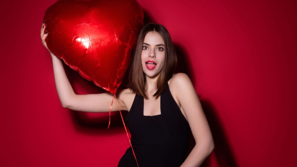 mulher branco usando um vestido e segurando um bolão de coração vermelho em fundo vermelho