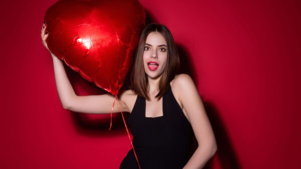 mulher branco usando um vestido e segurando um bolão de coração vermelho em fundo vermelho