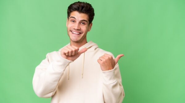 homem jovem sorrindo e apontando os dedos para trás em fundo verde