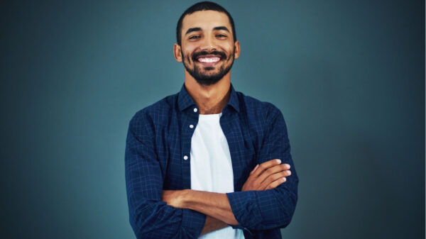 Retrato de um homem de braços cruzados, feliz, sorrindo e confiante em um estúdio, isolado em um fundo escuro.