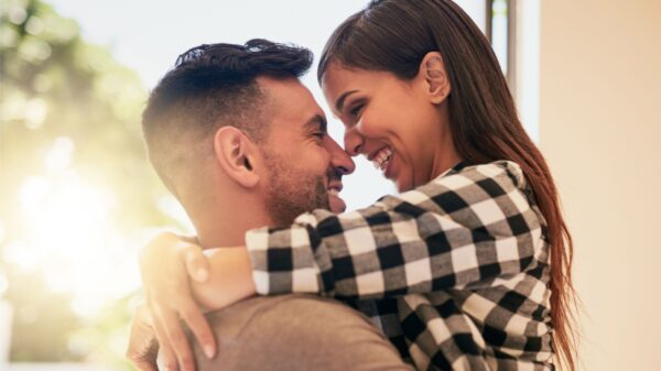 casal abraçados com os rostos colados um no outro em um lugar aberto