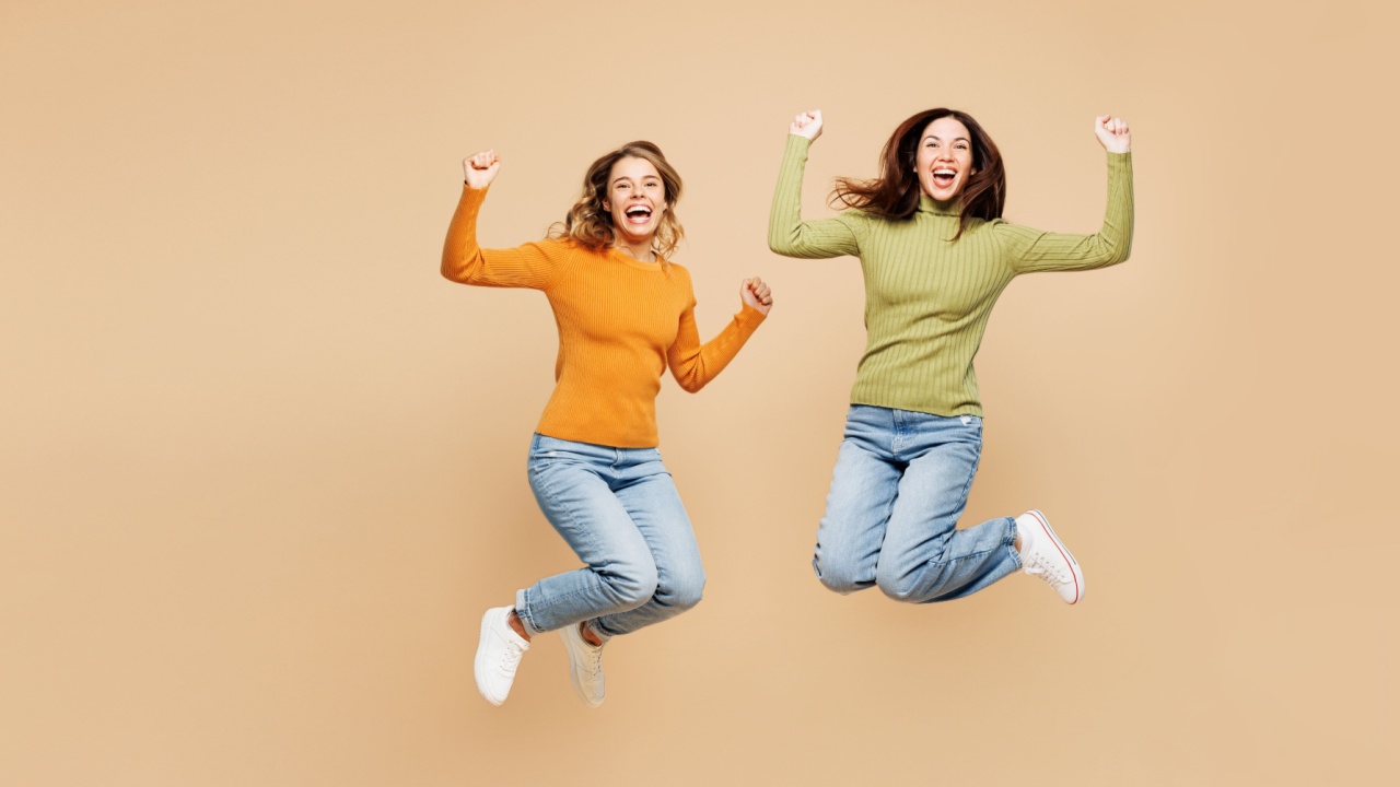 duas amigas jovens pulando em um fundo marrom