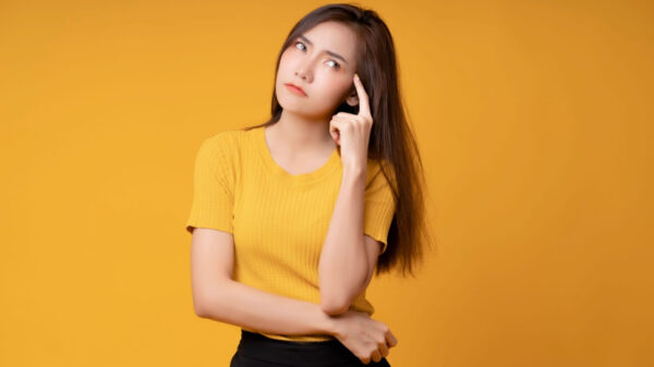 Mulher pensando, usando uma blusa amarela em um fundo amarelo.