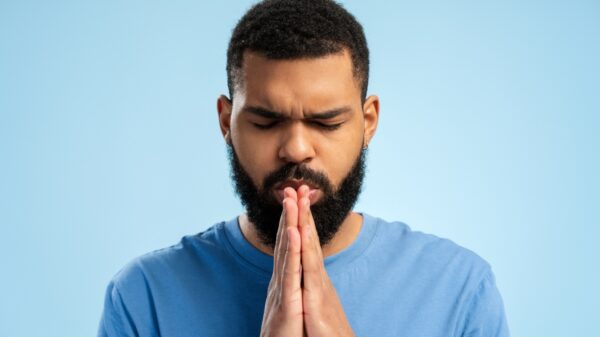 fotografia de um homem negro em oração vestindo roupa azul em fundo azul claro