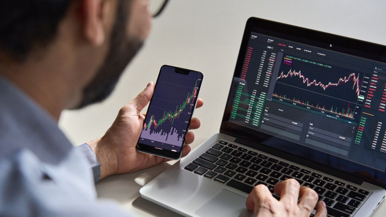 fotografia de um homem vendo finanças no notebook e no celular