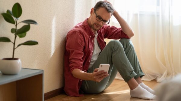 homem sentado no chão com expressão de nervosismo e segurando um celular