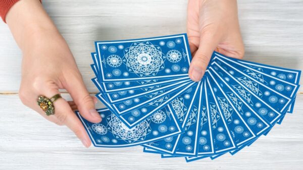 mão feminina branca segurando um baralho de tarot na cor azul em cima de uma mesa de madeira branca