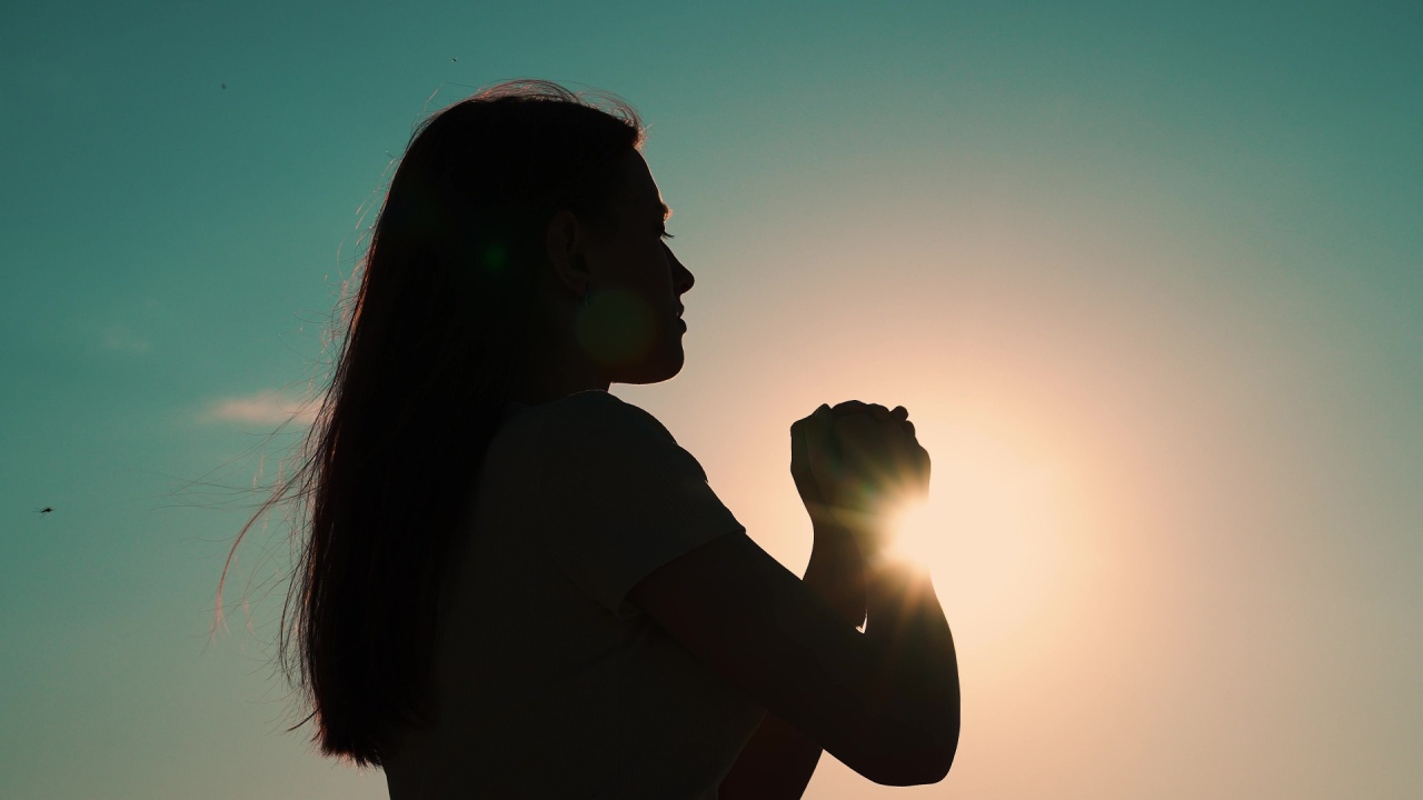 mulher fazendo oração contra luz em sombra com o sol