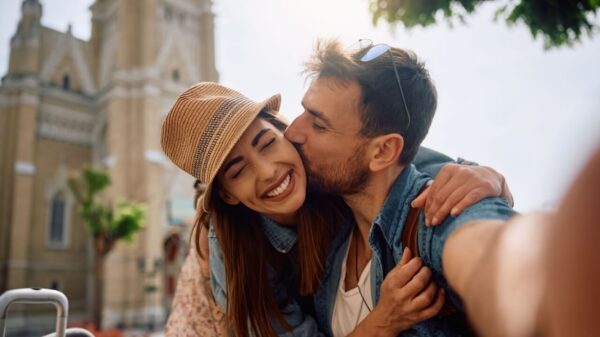 casal tirando uma foto dele dando um beijo na bochecha dela em uma viagem