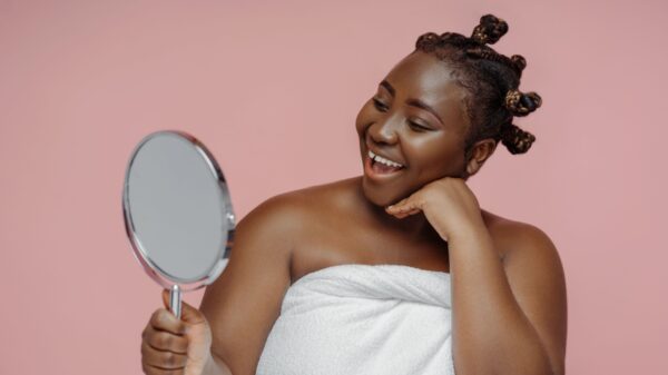 mulher negra sorrindo segurando um espelho em fundo rosa