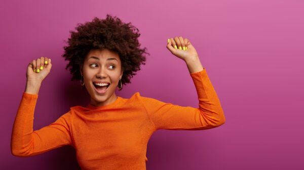 mulher negra usando roupa laranja e comemorando em fundo magenta