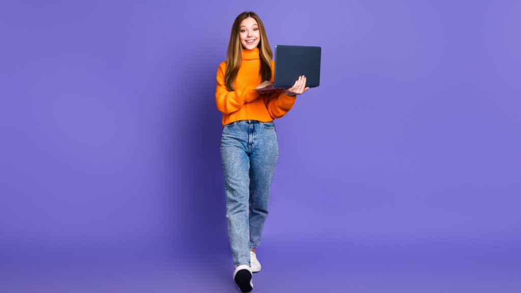 menina vestida com roupa laranja segurando um notebook em fundo roxo