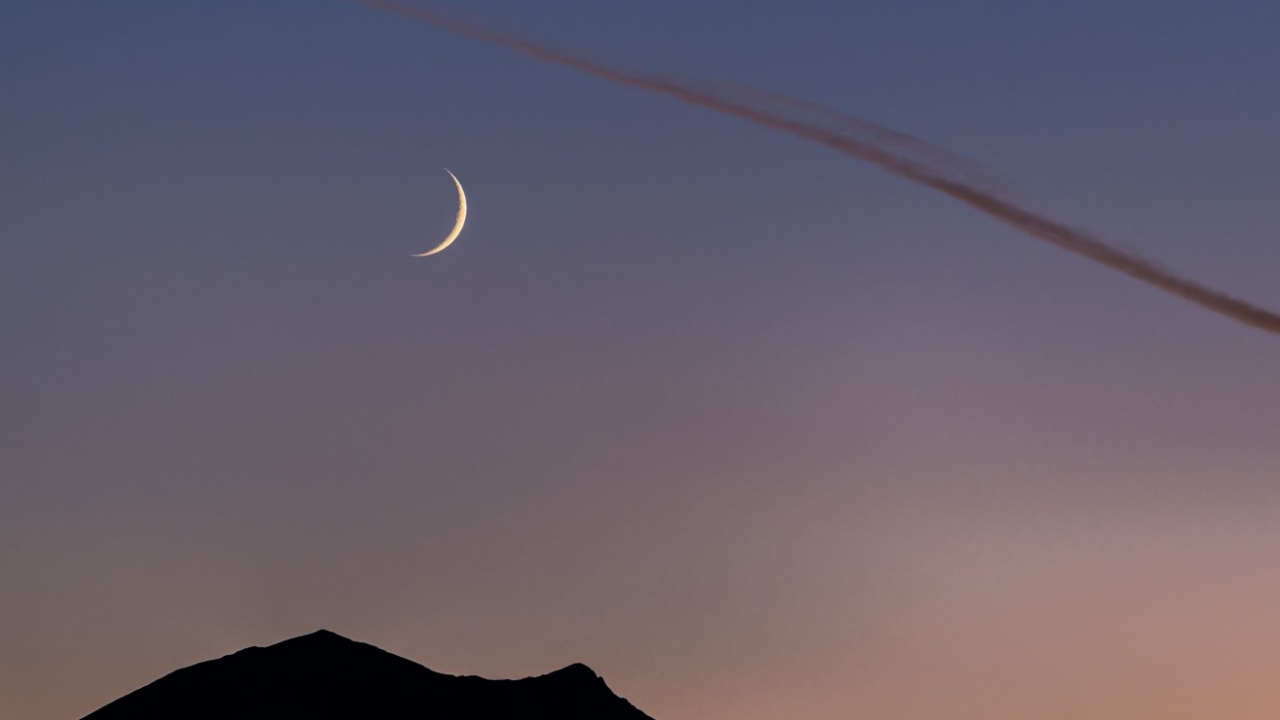 imagem de uma lua crescente vista em cima de montanhas