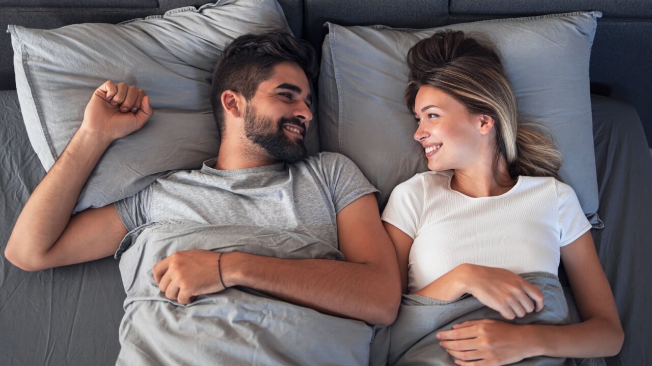 casal sorrindo deitados na cama e se olhando