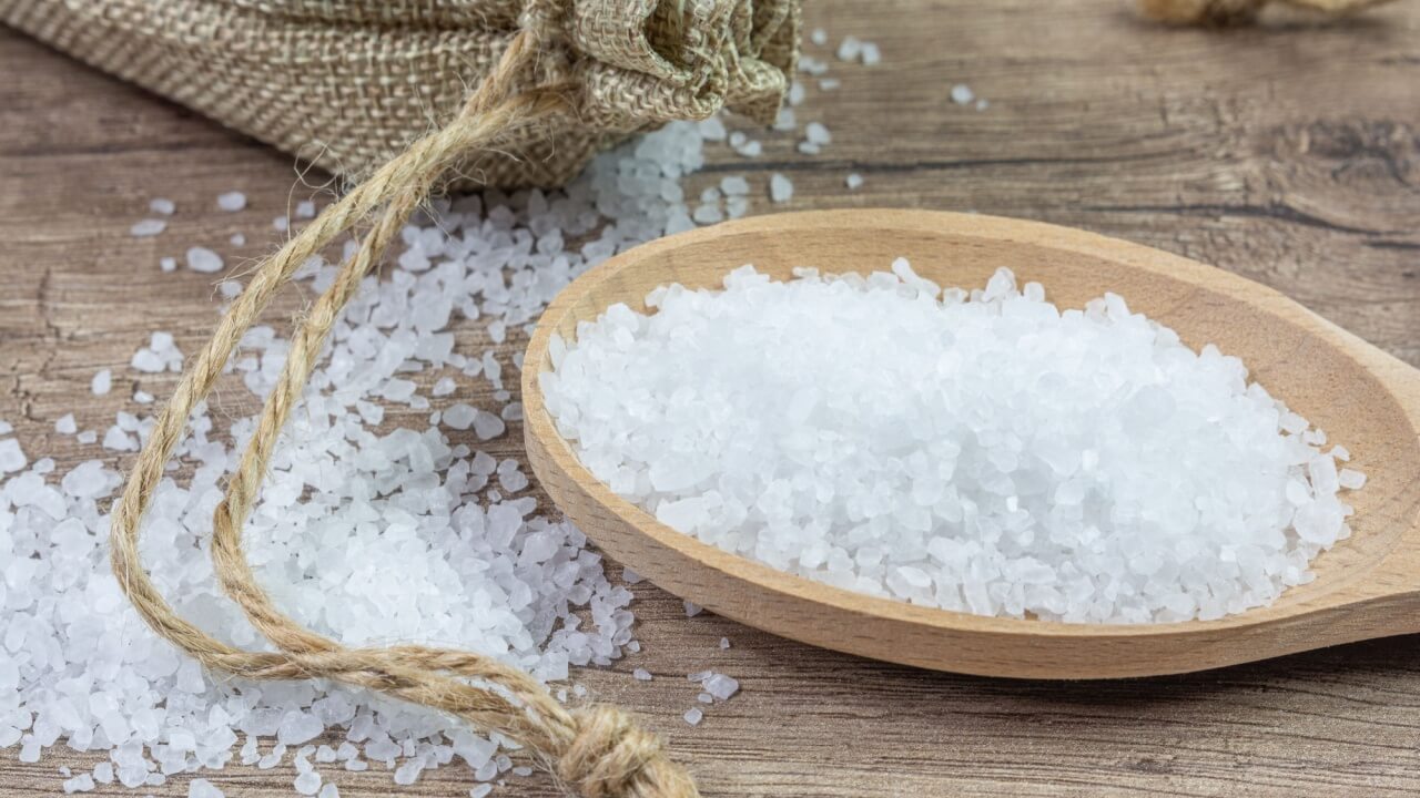 dois punhados de sal grosso em cima de uma mesa e um recipiente de madeira