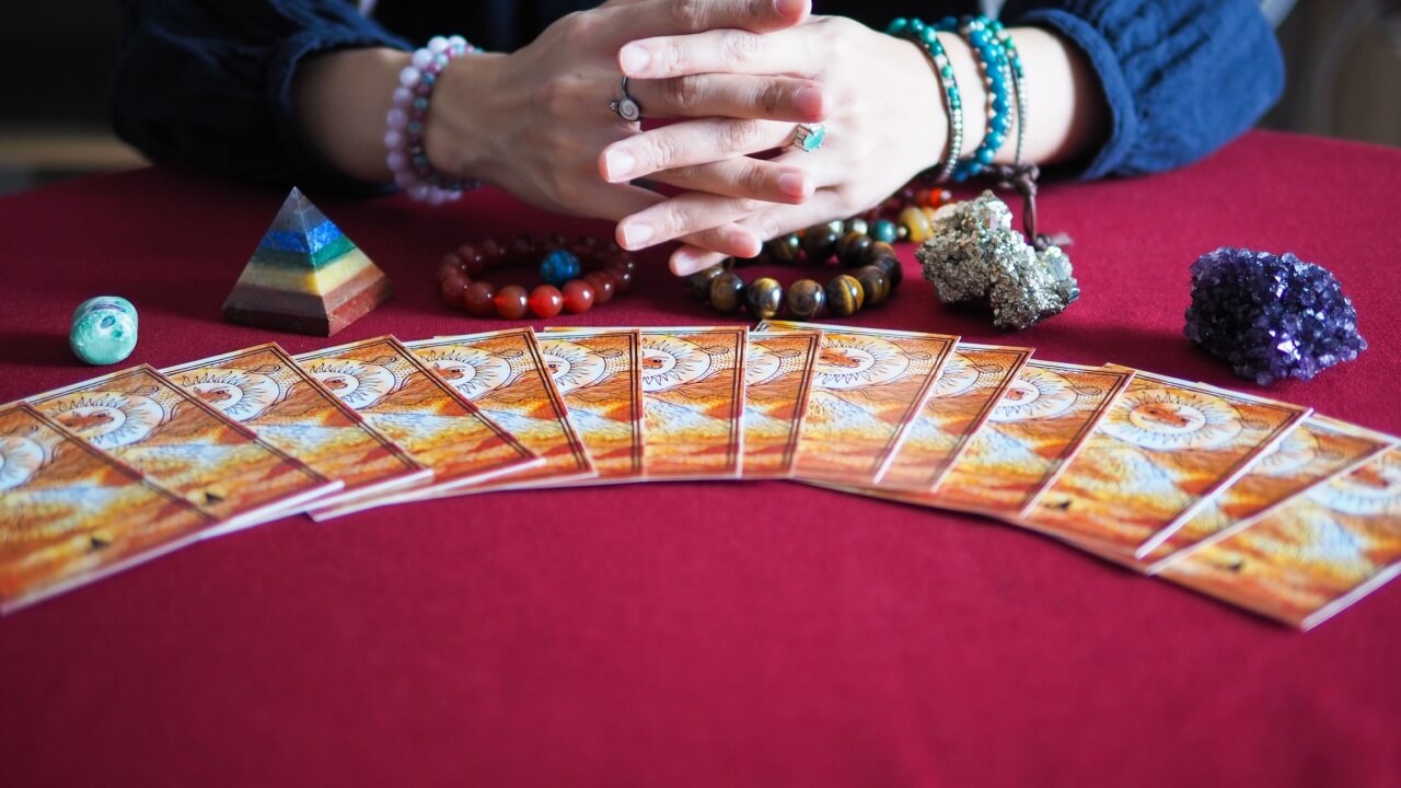 par mãos femininas juntas e um baralho de cartas a frente com toalha vermelha na mesa