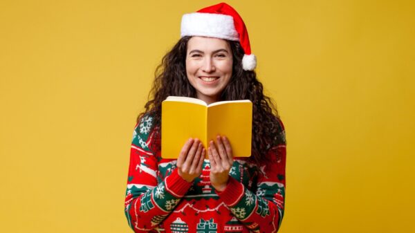 mulher com roupa natalina segurando um livro amarelo em fundo amarelo