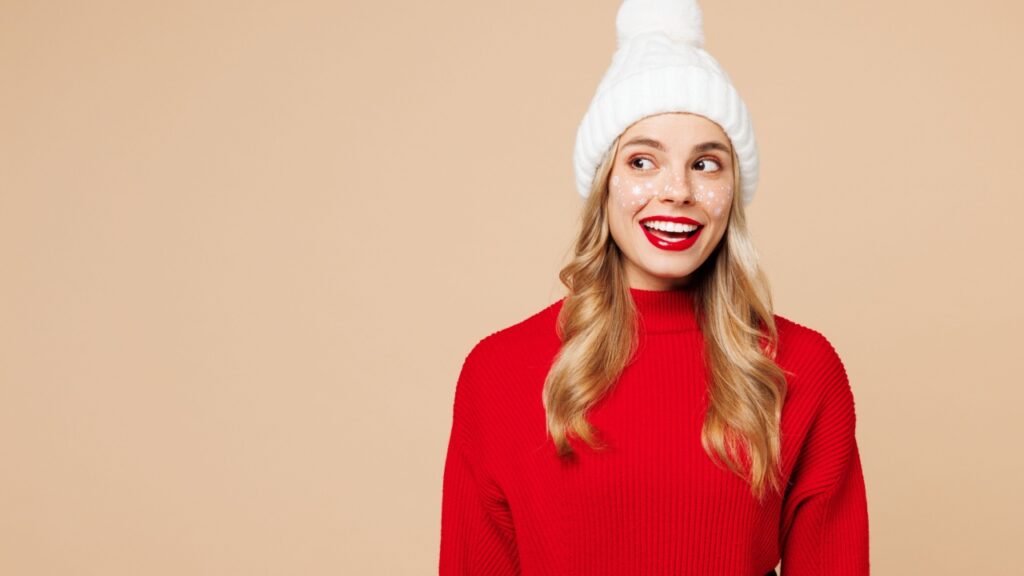 mulher com gorro de natal e blusa de lã vermelha em fundo salmão