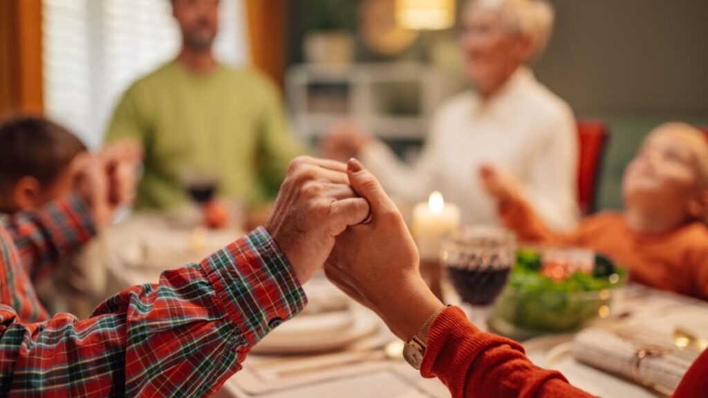 foto das mãos de pessoas sentadas ao redor de uma mesa orando