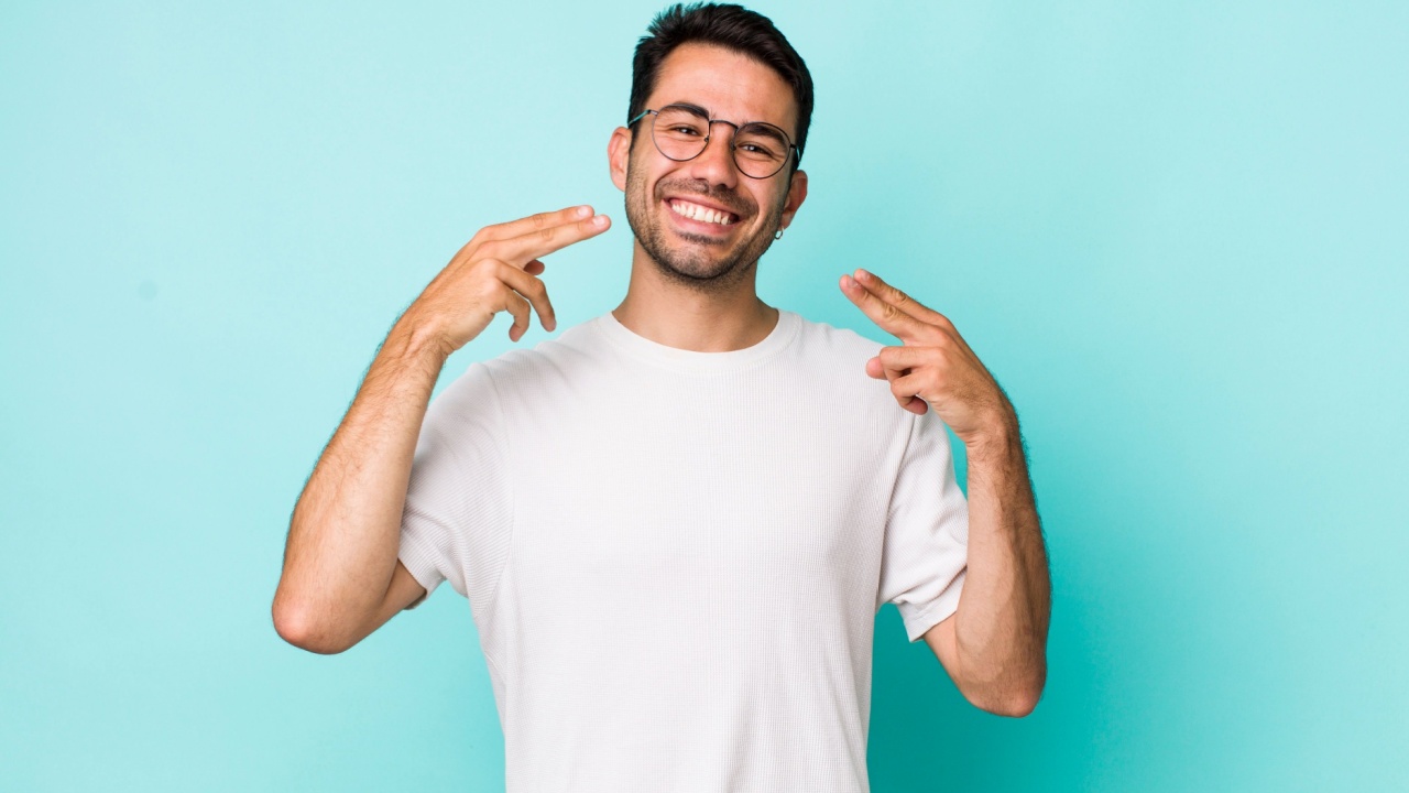 homem sorrindo e apontando para o próprio sorriso em fundo azul claro