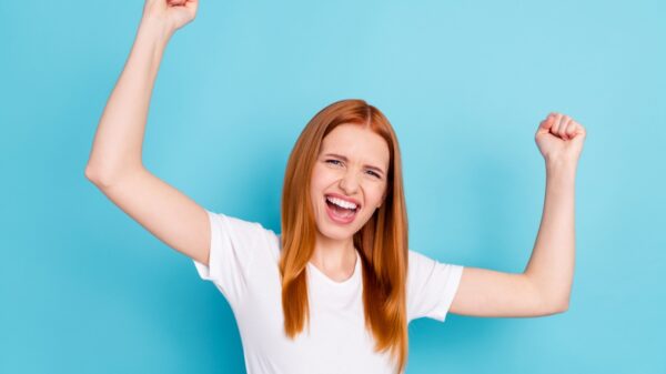 mulher com os braços para cima comemorando em fundo azul - Foto: Shutterstock